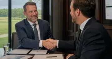 Professioneller Handschlag zweier Herren im Golfclub-Boardroom mit Golfplatz im Hintergrund